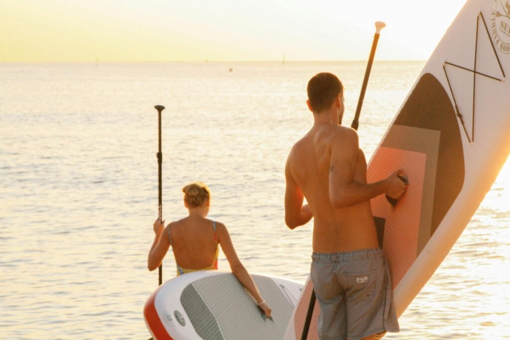 2-people-carrying-paddleboards A woman and a man each carrying a paddleboard towards the water