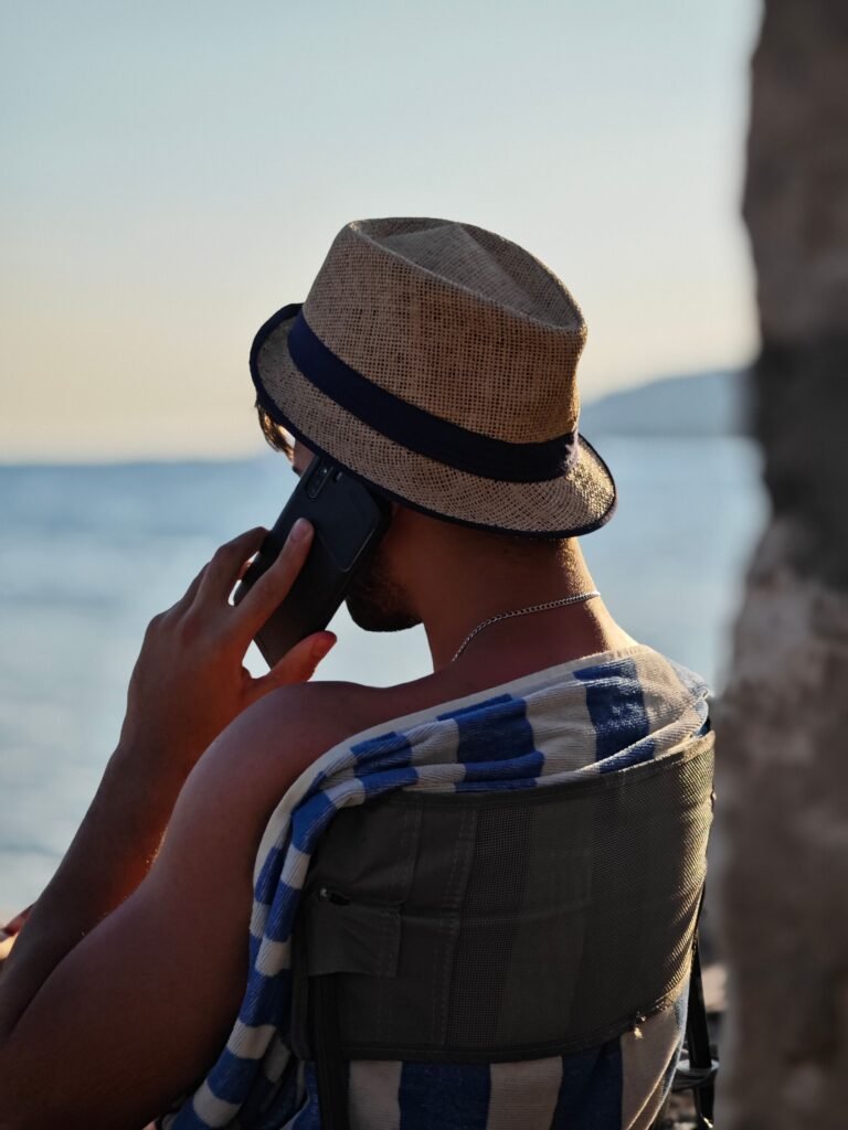 pexels-photo-27540545-27540545 A man relaxes on a beach chair while talking on his phone by the ocean's edge.